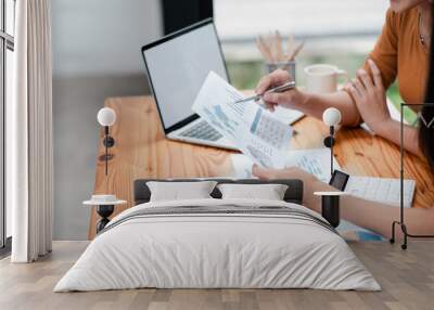 Two colleagues reviewing financial charts and graphs at a wooden desk in a contemporary office environment. Wall mural