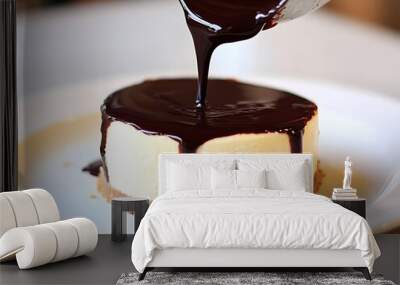 A close-up of a cheesecake topped with rich chocolate sauce being poured from a silver pitcher. Wall mural