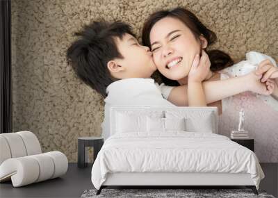 Asian family mother and son happy kiss love together lying down on carpet floor, parent and kid is real people family. Wall mural