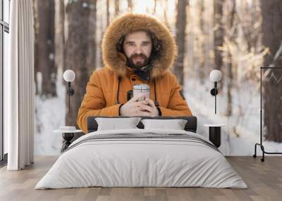 Close-up portrait handsome bearded millennial man in winter clothes and with thermos snow outdoor. Cold season and hot beverage in winter time, Copy space Wall mural