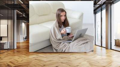 Freelance, freedom and people concept - Young woman with cup of hot drink sitting on floor and working at laptop at home Wall mural