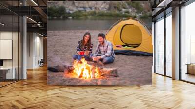 People, tourism and nature concept - Man embrace woman sitting near a fire Wall mural