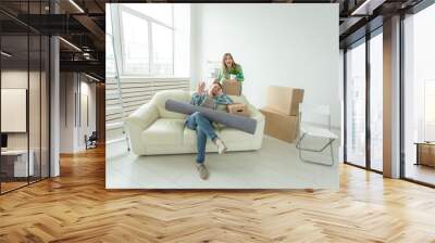 Satisfied cheerful young couple strong man and pretty woman holding their things in their hands sitting in the living room of a new apartment. Housewarming concept. Wall mural