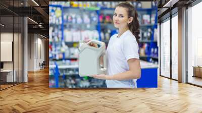 A young girl saleswoman offers a choice of engine oil for the engine in an auto parts store Wall mural