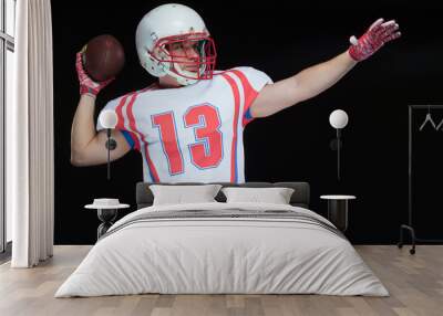 Front view of American football player wearing helmet throwing ball standing against black background Wall mural