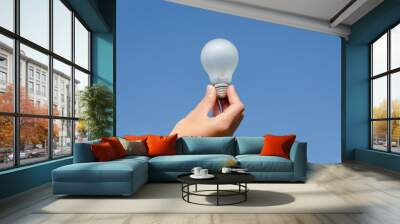 hand hold light bulb on blue sky background Wall mural