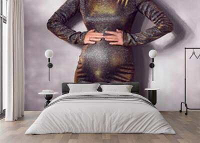 Trendy stylish beautiful pregnant woman in a tight silver sequined dress against a white wall background. Vertical Wall mural