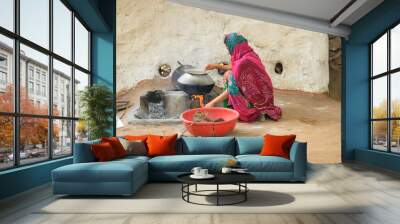 A woman cooking food in a stove made of mud. Wall mural