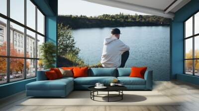 A man sits in front of a lake in the mountains and enjoys the view. Wall mural