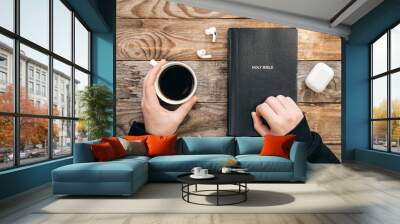 Bible, earphones and a cup of coffee in male hands on a wooden background, top view, the concept of religious, christian literature and Bible study. Wall mural