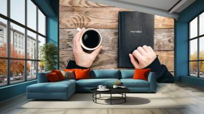 Bible and a cup of coffee in male hands on a wooden background, top view, concept of christianity and religion. Wall mural