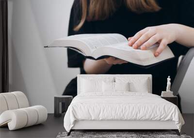 Christian girl holds Holy Bible in hands in a sunny room, close up. Wall mural