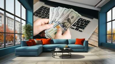 Paper dollar bills in the hands of a man against the background of a laptop, close-up, online earnings, a trader makes money on the Internet. Wall mural