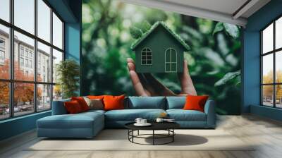 A hand holding up a miniature green house, symbolizing environmental responsibility and sustainable living. Wall mural