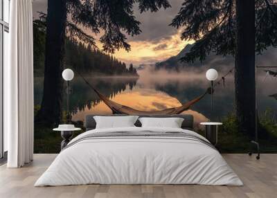 A peaceful summer camping scene by a lake with an empty hammock between two trees, and a foggy mountain lake at sunrise Wall mural