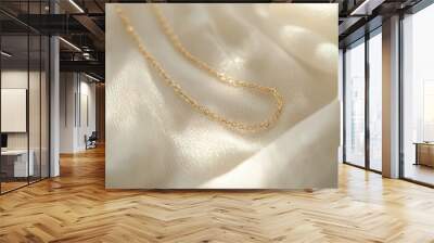 Close-up of a delicate gold chain necklace resting on white textured fabric, shimmering in soft light Wall mural