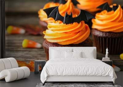 Cupcakes with bat decorations and bright orange frosting, placed on a rustic wooden table, fall leaves and candy corn adding a festive touch Wall mural