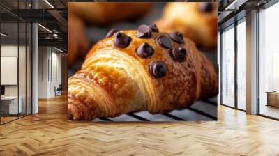 Freshly baked chocolate chip croissants, golden brown and flaky, resting on a cooling rack. The chocolate chips are melted and gooey, promising a sweet and indulgent treat. Wall mural