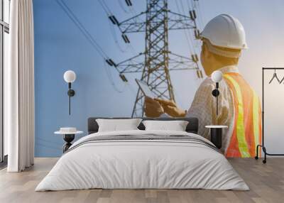 Electrical engineer holding and using a digital tablet with high voltage tower background. Wall mural