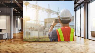 Engineers use mobile phones to photograph high-voltage electricity poles against sub-station background. Wall mural