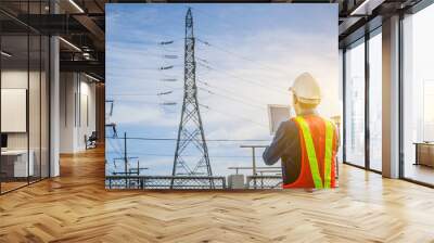 Engineers use the tablet at the high voltage pole against the blue background. Wall mural