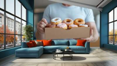 A man is holding a box of assorted donuts. Wall mural