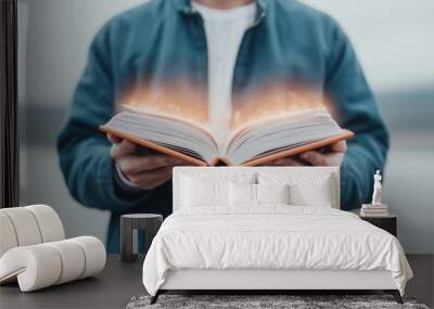 A man is holding an open book with a glowing light around it. Concept of wonder and curiosity, as if the man is about to embark on a journey of knowledge and discovery Wall mural