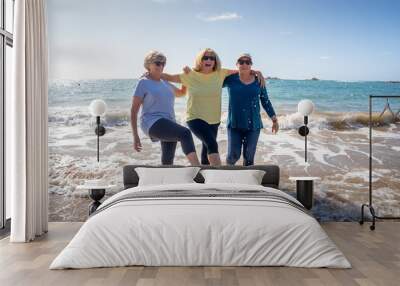 Group of three senior women walking having having fun on beach. Friendship and healthy lifestyle Wall mural