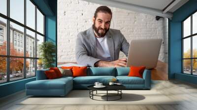 Portrait of happy attractive young businessman working on laptop looking confident Wall mural