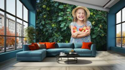 Happy little girl holding apples in the garden Wall mural