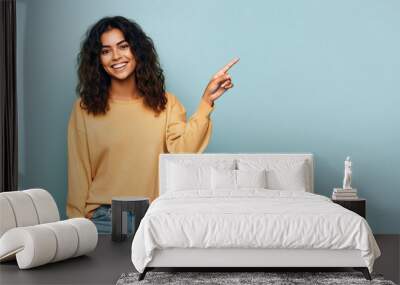 Young woman pointing finger to side, latin girl isolated on blue Wall mural