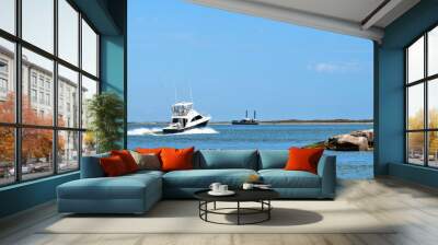 Broadside view of a beautiful white and black fishing yacht boat sails past rock breakwater on the calm blue water on a sunny day. Wall mural