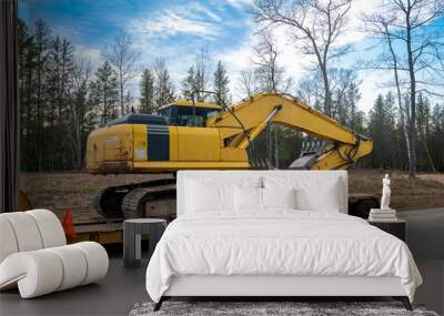 Used Yellow Skid Steer Excavator Loader on a flat bed trailer, at a construction job site, in evening light with trees in the background. Wall mural