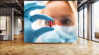 Young attractive female scientist holding a red transparent pill Wall mural