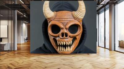 A detailed wooden mask with horns and a fierce expression on a person wearing a dark hoodie. Wall mural