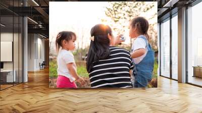 Asian little child girl drink water from bottle after tired of playing in the garden with mother and sister, looking sunset in evening. Wall mural