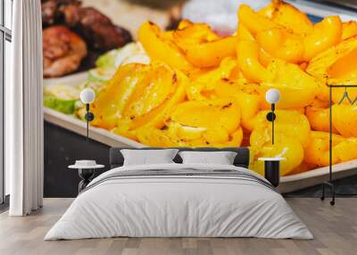 A tray of yellow peppers sits on a table next to a plate of meat Wall mural