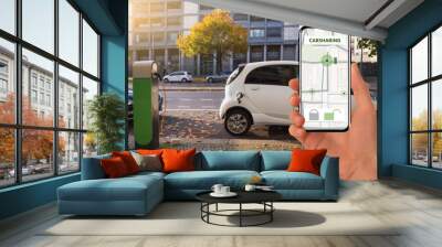 Hand with a mobile phone on the background of a charging carsharing electric car Wall mural