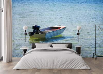 A small boat with outboard motor anchored in shallow calm clear water on a sunny summer day. Copy space. Wall mural