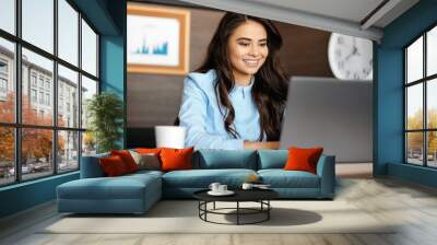 Photo of beautiful young manager woman with bright smile working with laptop in modern office. Wall mural