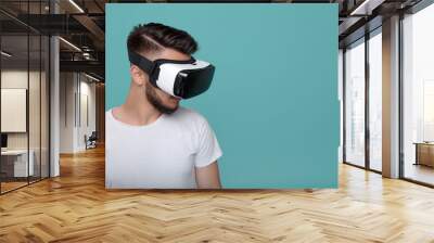 Young handsome bearded man looking down with virtual reality goggles in studio on colorful background. Smartphone using with VR headset. Wall mural