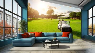 Golf cart in fairway of golf course with green grass field with cloudy sky and trees at sunset Wall mural