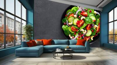 Spinach salad with fresh cucumbers, tomato, onion, pomegranate, sesame seeds and cashew nuts on black background. Healthy vegan food. Top view. Banner Wall mural