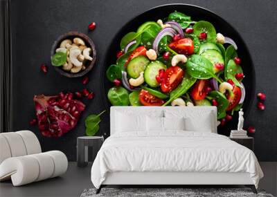 Spinach salad with fresh cucumbers, tomato, onion, pomegranate, sesame seeds and cashew nuts on black background. Healthy vegan food. Top view Wall mural