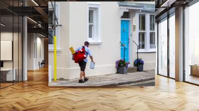 A postman or mail man carrying a mail bag delivering post to english homes Wall mural