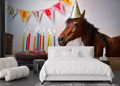 a horse wearing a colorful party hat looks at a chocolate cake with lit candles symbolizing celebration joy festivities birthday and animal happiness Wall mural