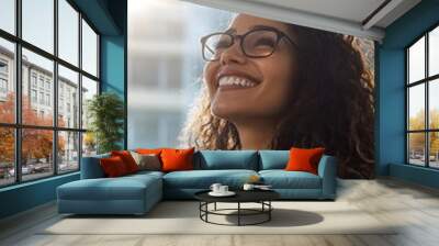 A smiling businesswoman with glasses in an office setting, looking up at the sky and enjoying life Wall mural