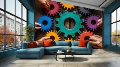 Diverse hands collaborating to assemble colorful gears on a wooden table. Wall mural