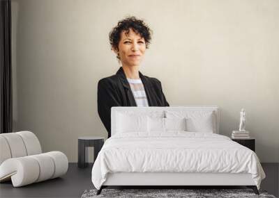 Portrait of smiling mature business woman standing arms crossed against wall Wall mural