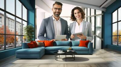 Smiling two professional business people standing in office with with digital tablets and looking at camera Wall mural